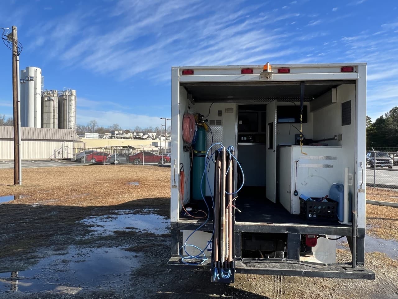 The GeoImaging data acquisition truck parked with its rear doors open, showing the bench workstation, gas cylinders, hose reels, and drive rods stowed inside
